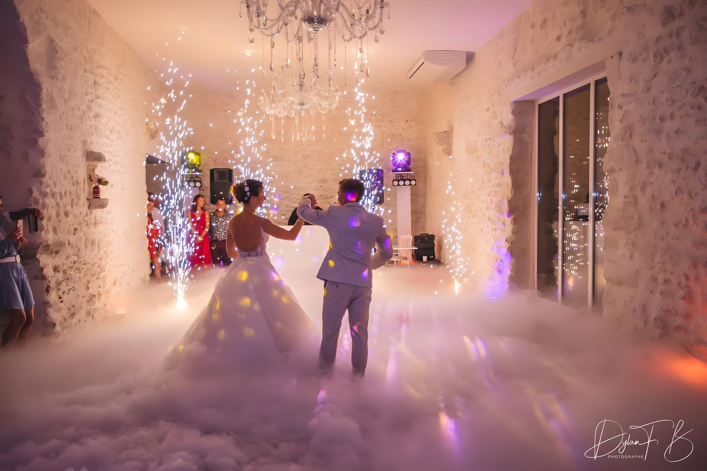 Les mariés dansent sur un tapis de fumée lourde sous un lustre en cristal, quatre jets d’étincelles froides le long des murs de pierre