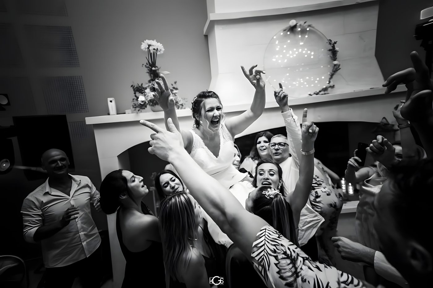 La mariée portée par ses invités au milieu de la piste, bras levés et mains ouvertes, en noir et blanc